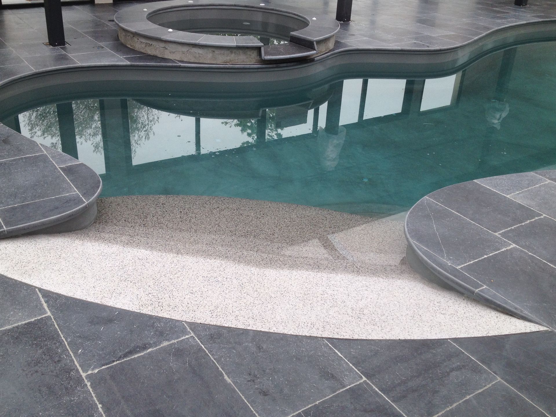 Piscine incurvée dans le jardin avec terrasse en pierre et zone peu profonde.