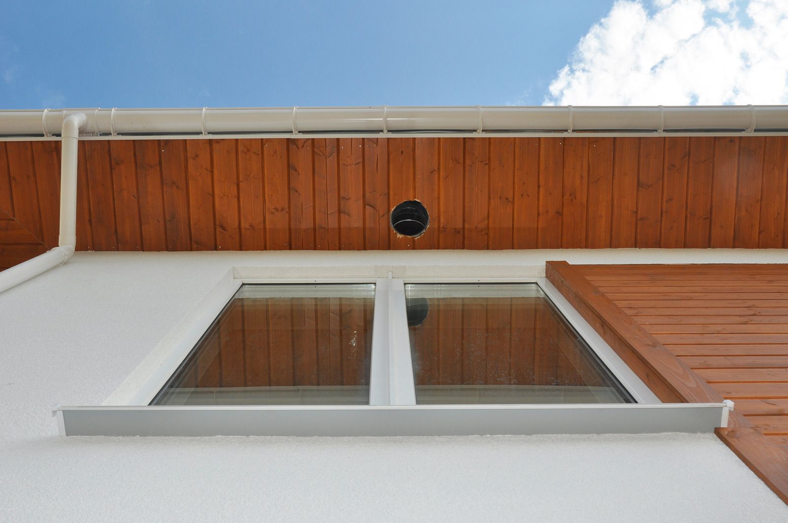 Looking up at a white building wall with a window and orange wood siding under a blue sky