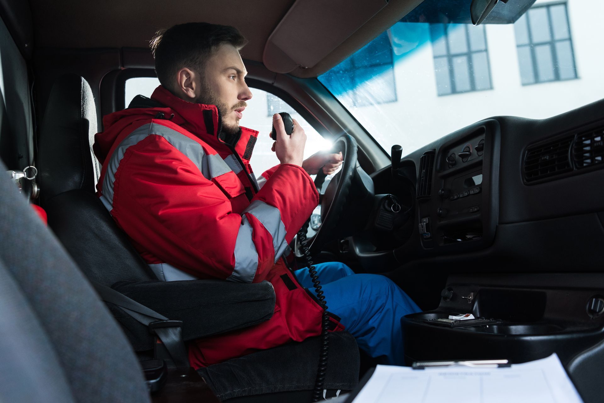 Un homme en veste rouge conduit un véhicule et parle dans une radio portative.