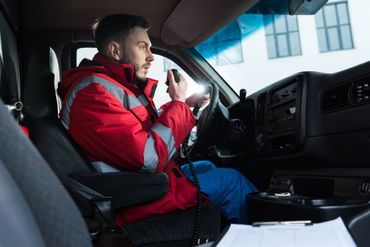 Un chauffeur en veste rouge parle à la radio dans la cabine de son véhicule.