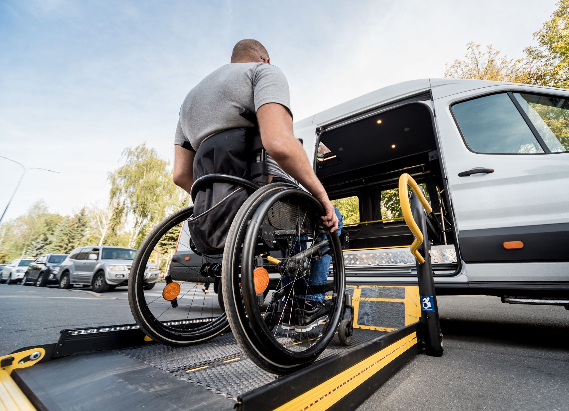 Une personne en fauteuil roulant monte à bord d'une camionnette grâce à une rampe déployée, un parking étant visible.