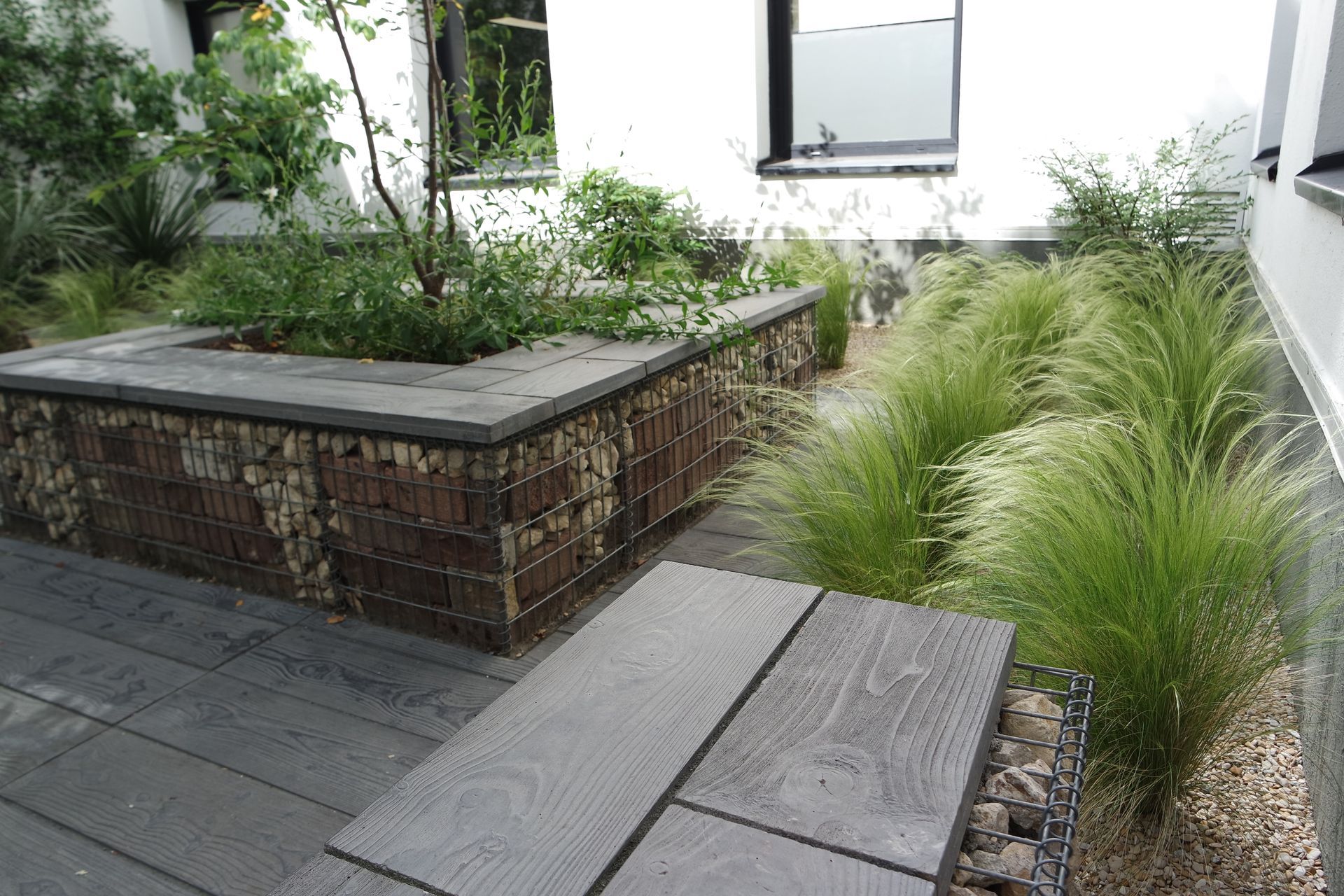 Jardin moderne avec des murs en pierre, du pavage en béton et des graminées ornementales.