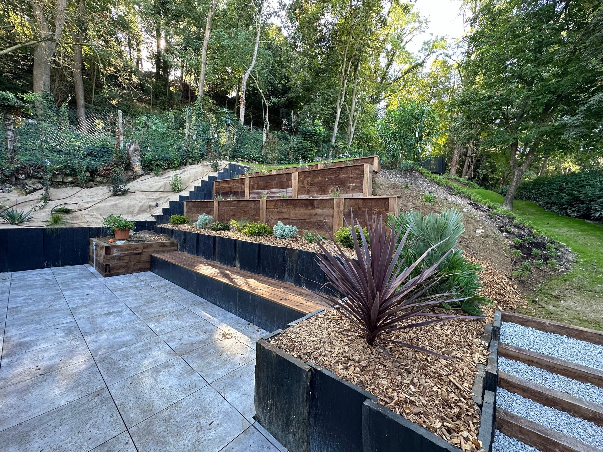 Jardin en terrasses avec des murs en bois, des plantes et une terrasse en pierre
