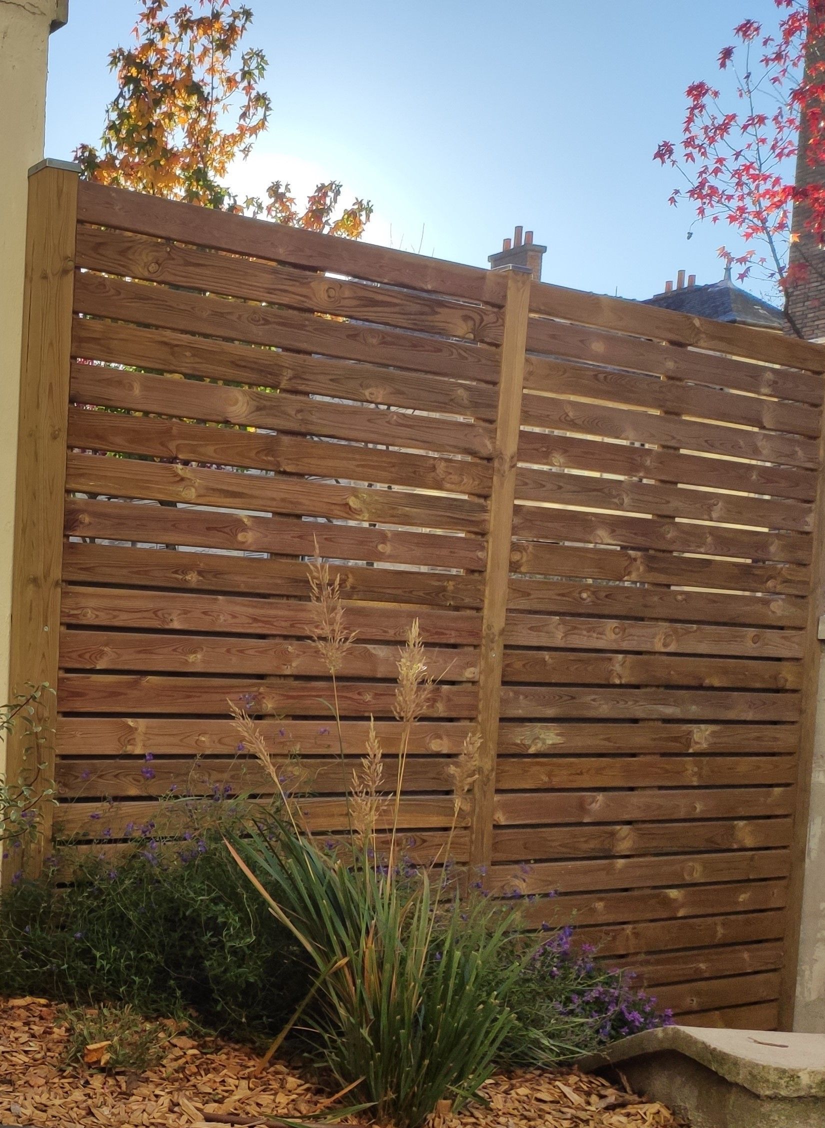 Clôture horizontale en bois dans un jardin planté et un ciel ensoleillé 