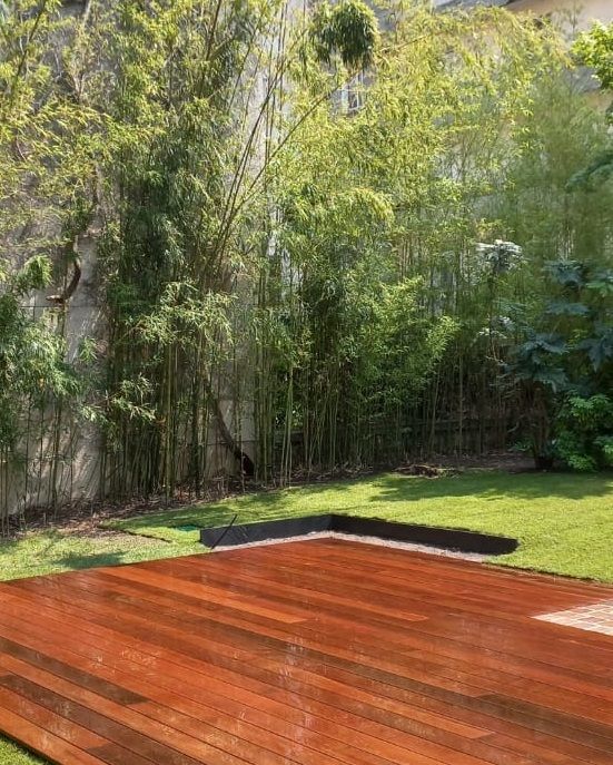 Terrasse en bois devant une bambouseraie et une cour herbeuse, avec un mur de pierre en arrière-plan