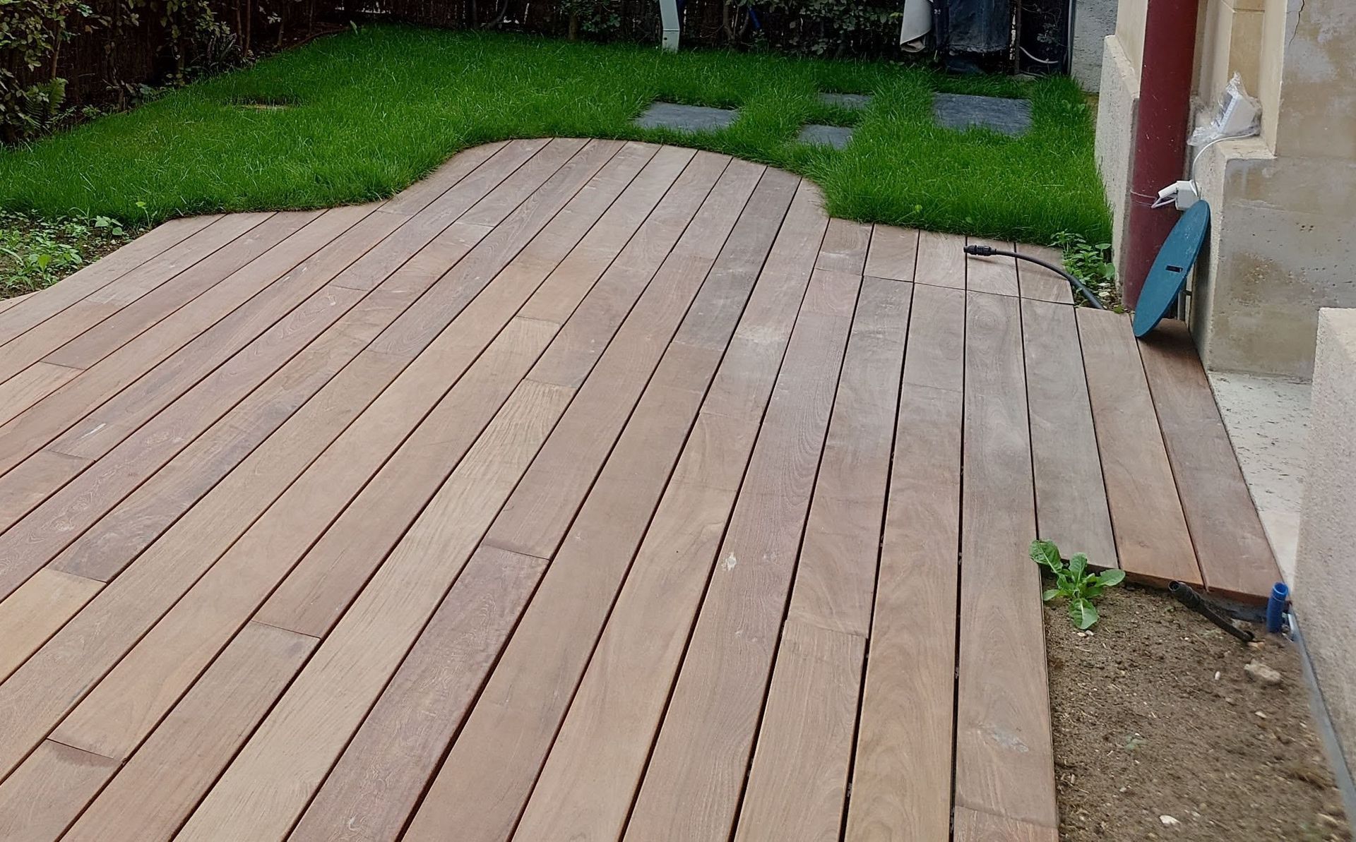Terrasse en bois avec un bord incurvé, à côté de l'herbe et d'un bâtiment