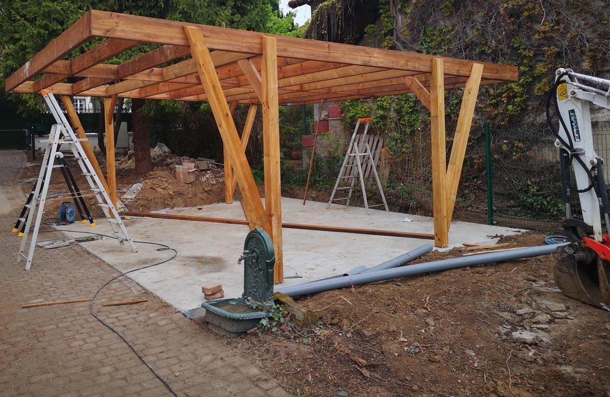 Abri en bois en construction sur une dalle de béton, des échelles, outils et terre entourent la structure