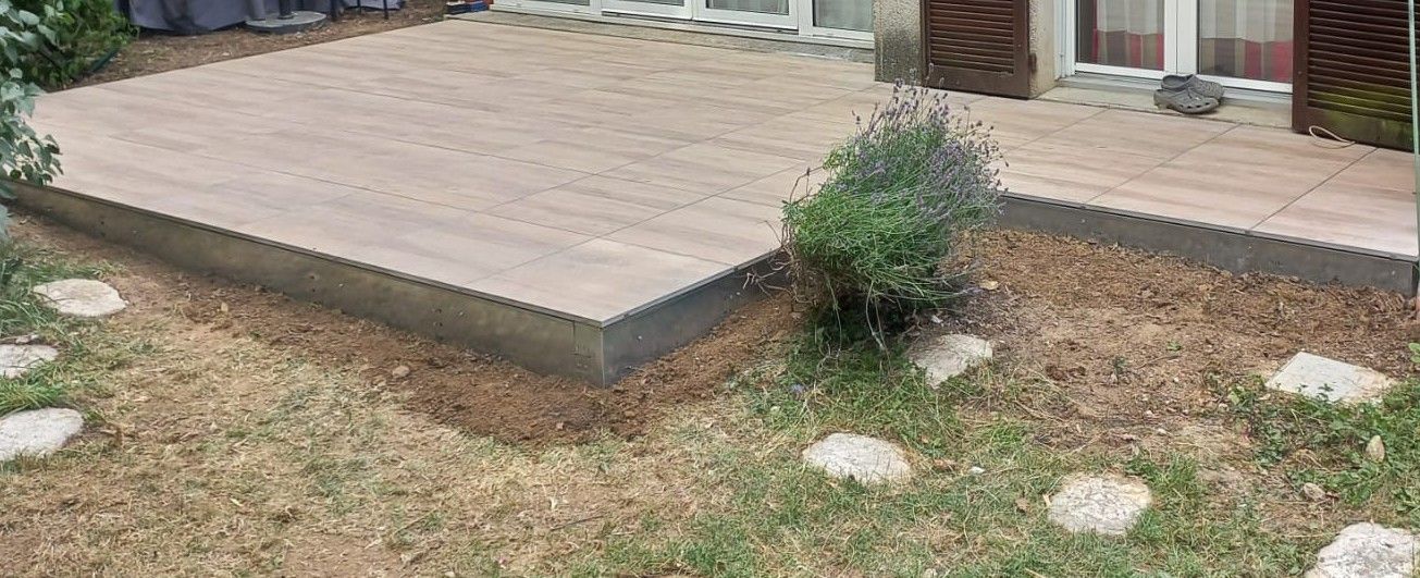 Terrasse en bois entourée de gravier et de plantes dans une cour avec peu d'herbe