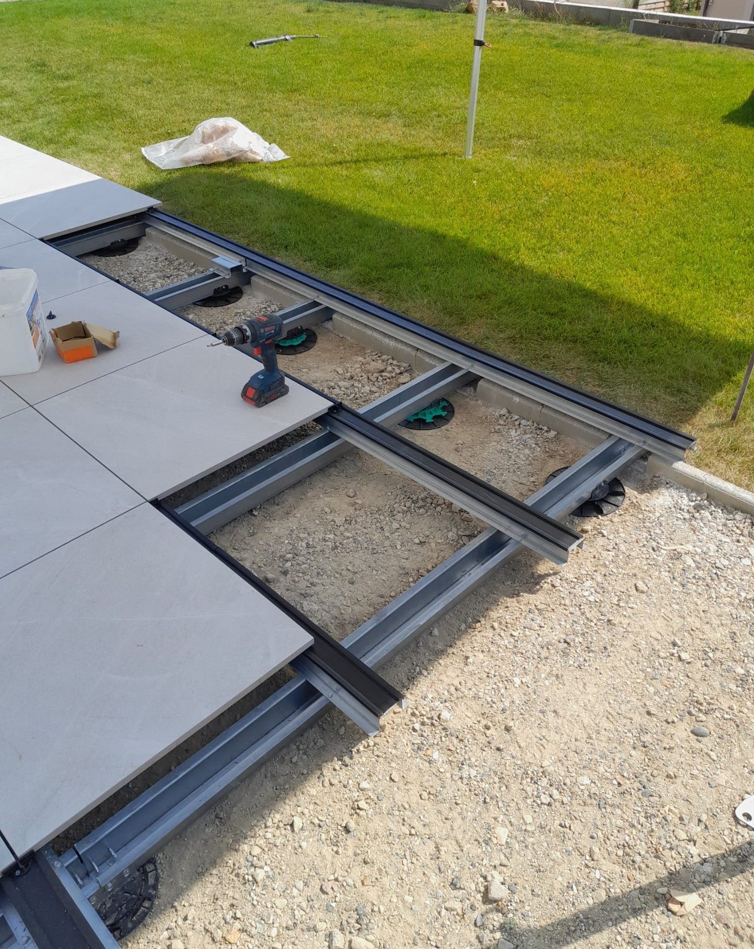 Pose de dalles de patio sur ossature métallique, base de gravier, en extérieur sur gazon avec perceuse électrique et outils visibles