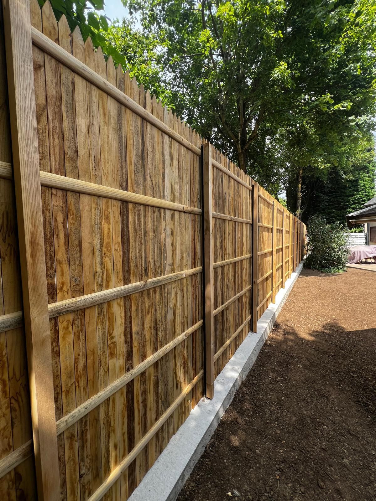 Clôture en bois avec des planches verticales et rails horizontaux, construite sur une fondation en béton, dans une cour