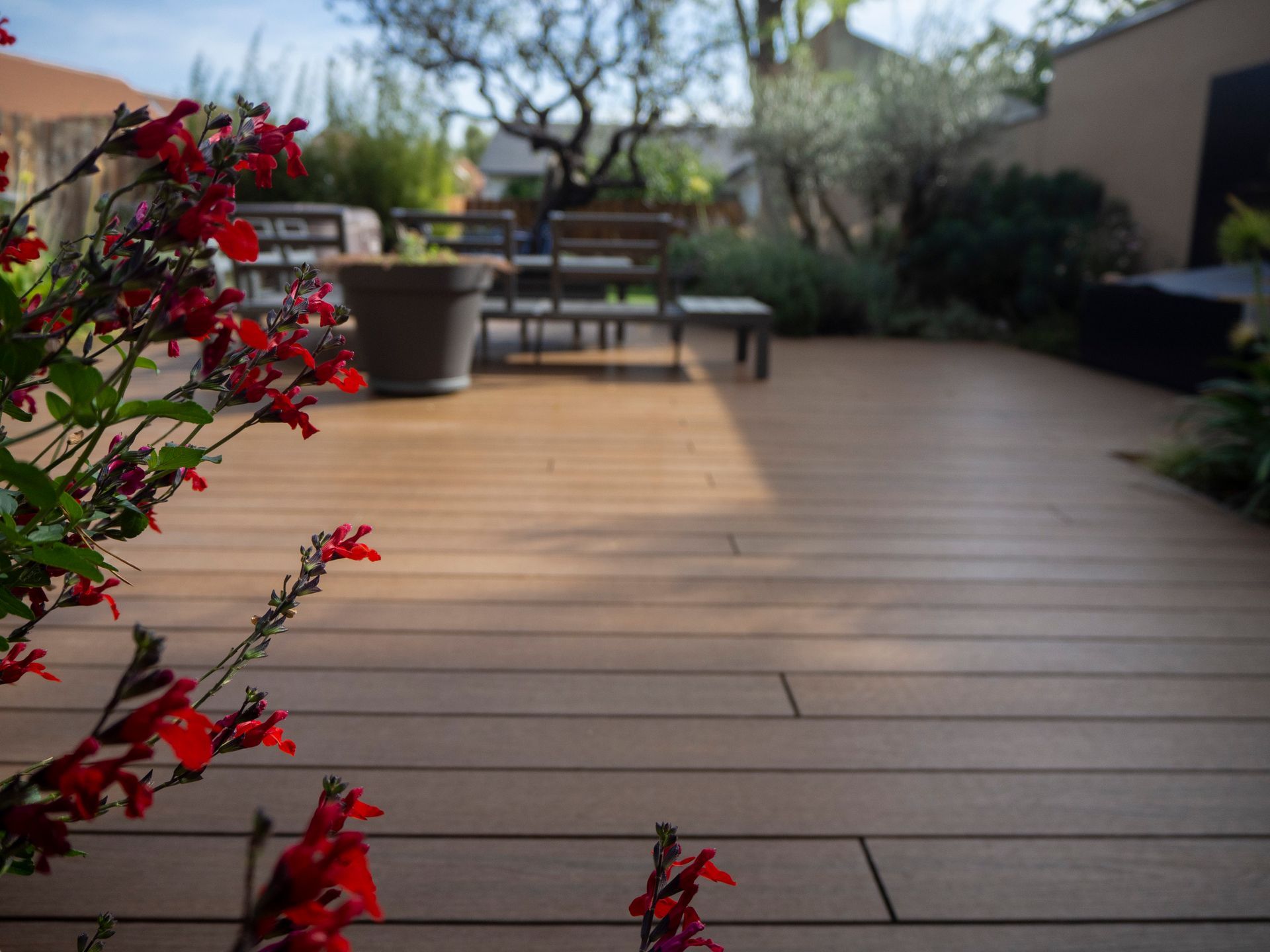 Terrasse en bois avec des fleurs rouges au premier plan, un coin salon avec une table et des chaises en arrière-plan flou