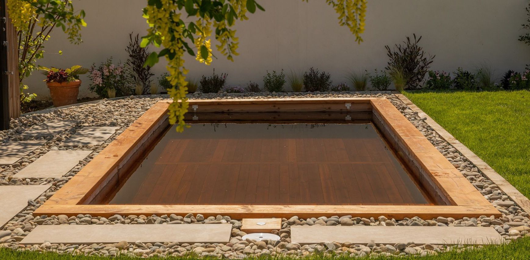 Une piscine rectangulaire à cadre en bois dans une cour arrière avec aménagement paysager en pierre et en herbe.