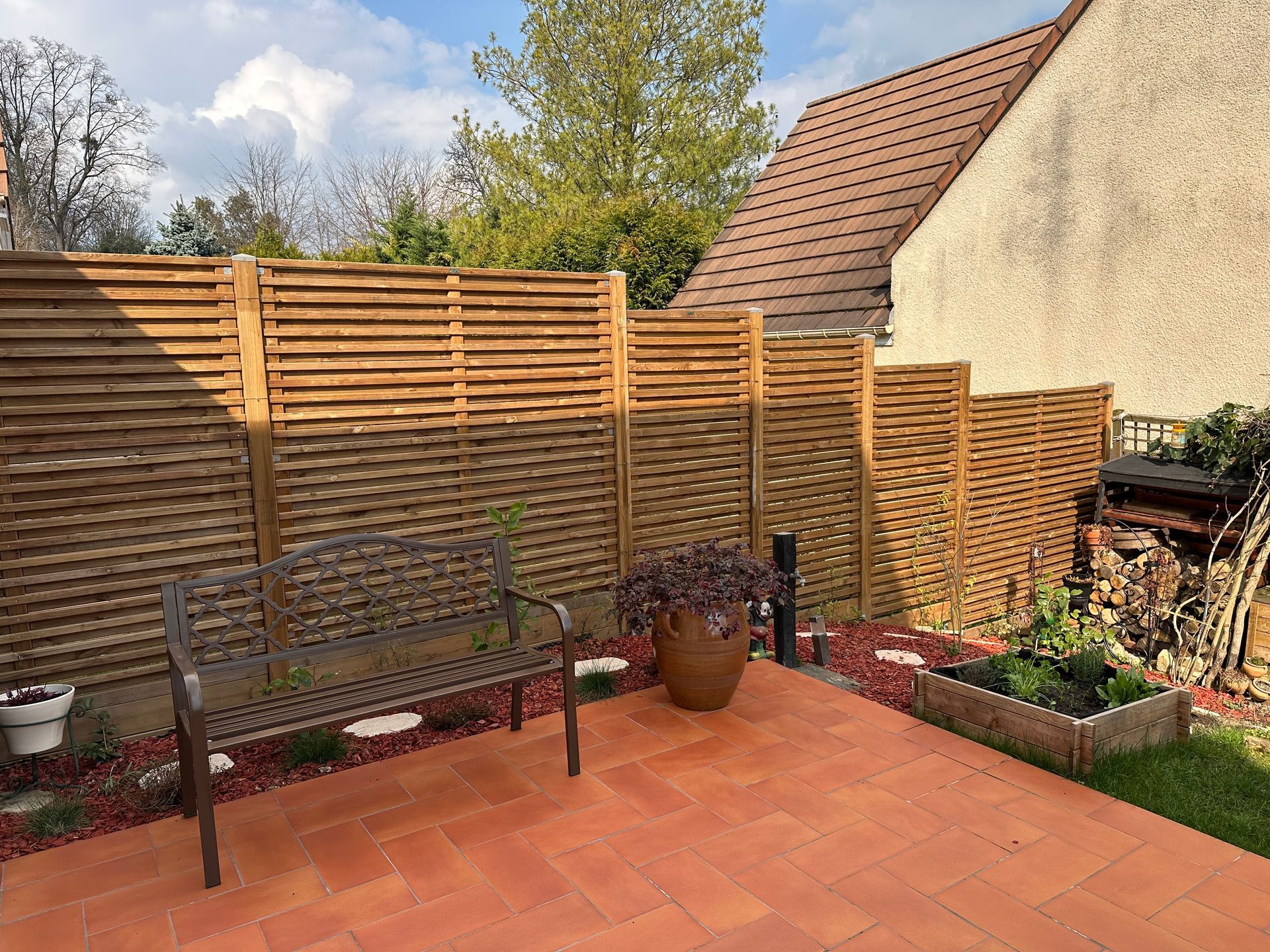 Patio arrière avec une clôture en bois,  un banc et des plantes