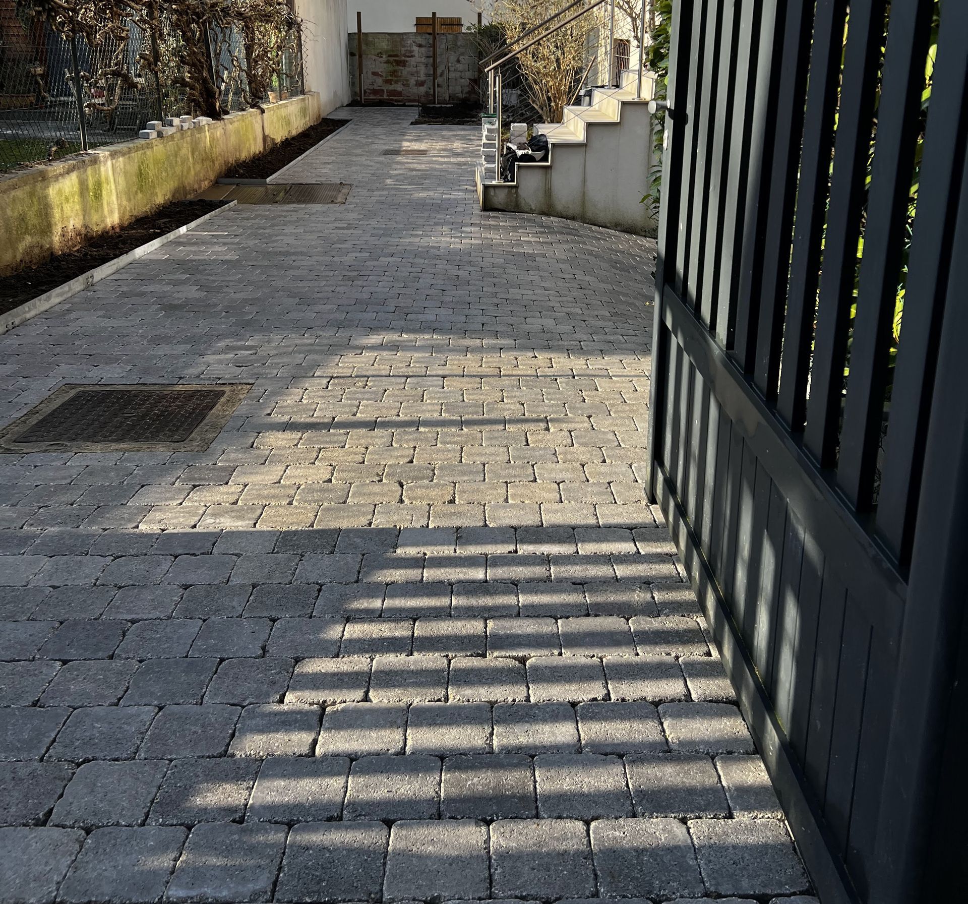 Allée pavée de pierres avec un portail projetant des ombres, menant à une maison à la lumière du jour