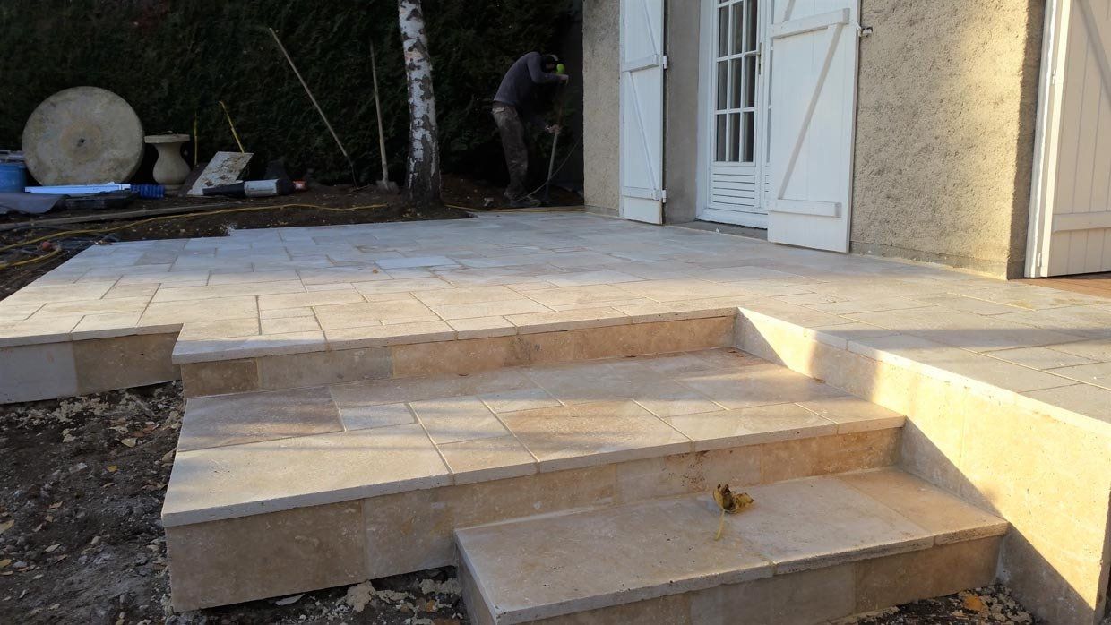 Patio en pierre avec marches menant à l'entrée d'une maison et une personne travaille en arrière-plan