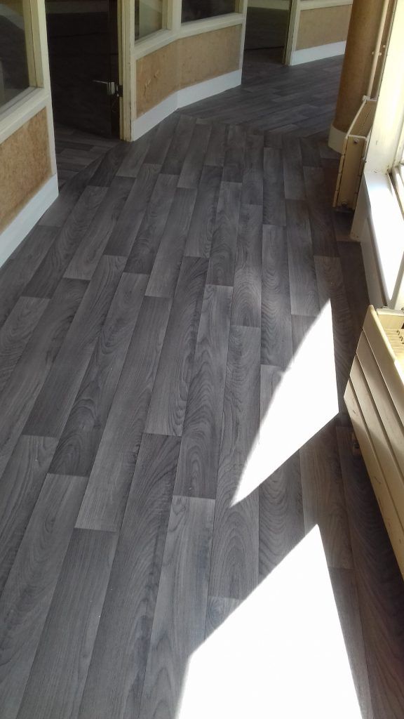 Parquet imitation bois gris dans un couloir incurvé, la lumière du soleil entrant par la droite.