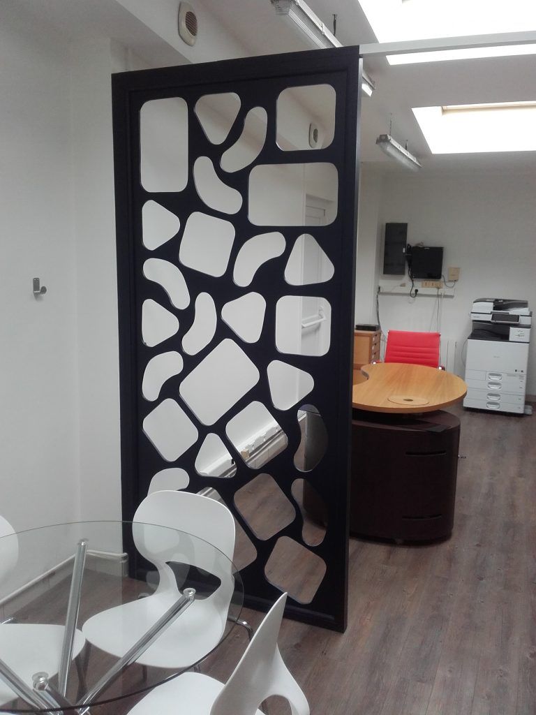 Cloison de séparation découpée noire avec des formes en miroir dans un environnement de bureau moderne avec tables, chaises et équipements.