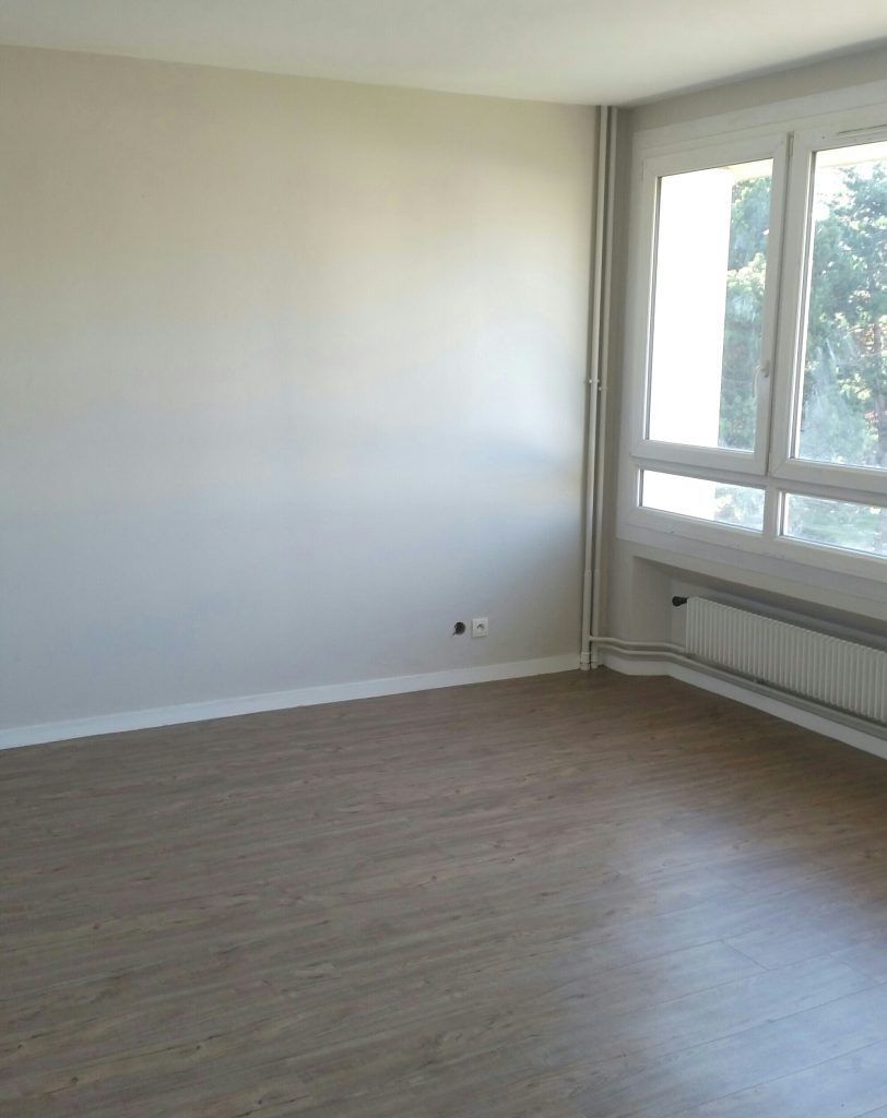 Chambre vide avec parquet, une fenêtre et des murs blancs.