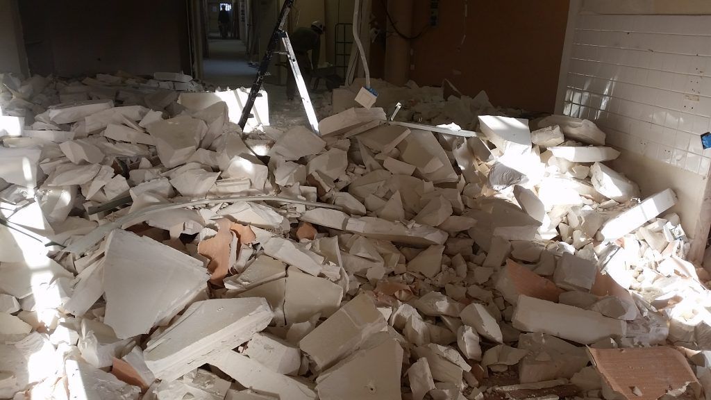 Tas de cloisons sèches et de débris démolis dans un couloir, éclairé par la lumière du soleil.