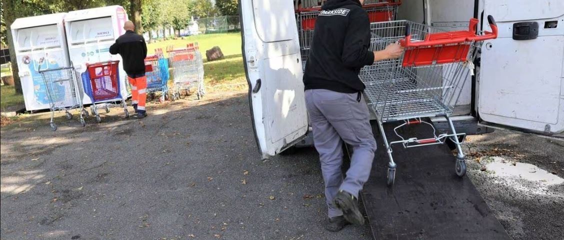 Un homme charge des chariots dans une camionnette. Les chariots sont sur une rampe. Deux autres hommes sont à proximité.