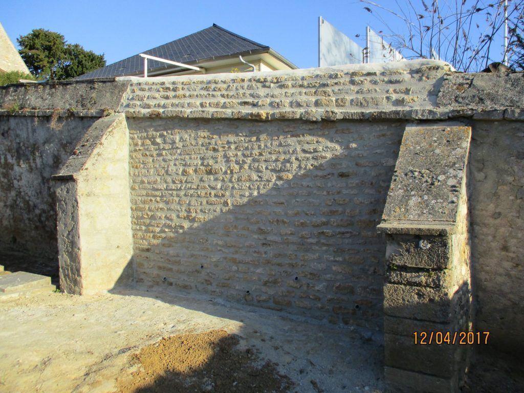 Mur de pierre avec piliers de soutien, peut-être extérieur d'un bâtiment, contre un ciel bleu.