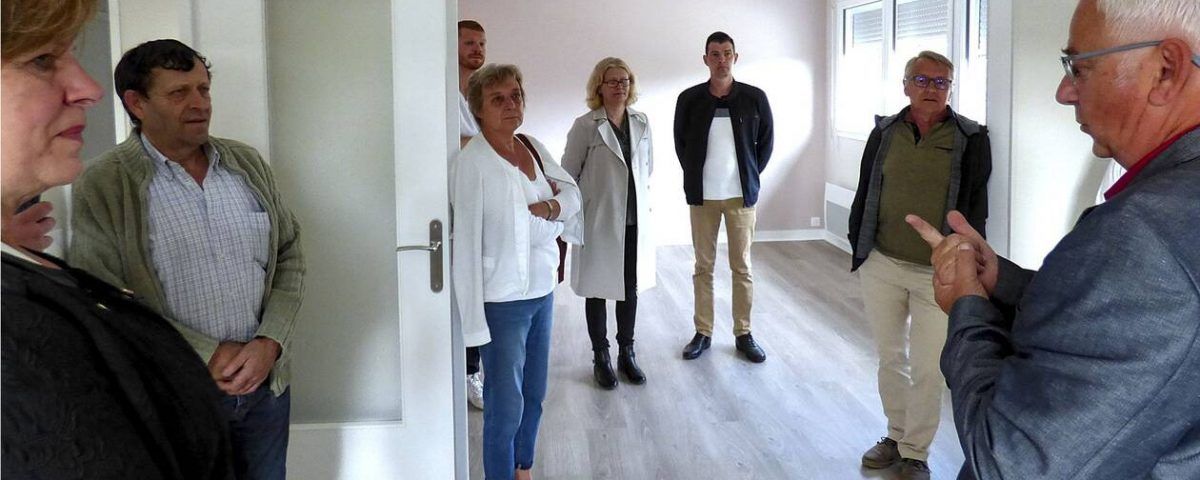 Un groupe de personnes dans une pièce très éclairée, écoutant un homme qui fait des gestes avec ses mains.