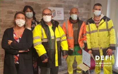 Groupe de six personnes portant des masques et des gilets de sécurité à l'intérieur avec le logo « DEFI ».