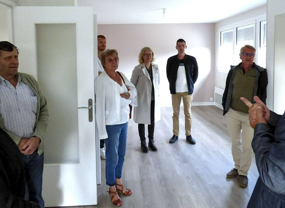 Un groupe de personnes dans une pièce lumineuse aux murs clairs et au sol gris. Certains observent, évaluent.