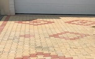 Allée en pavés de briques avec des motifs beiges et rouges devant une porte de garage blanche.