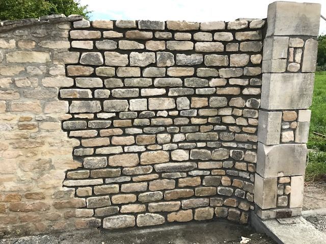 Construction d'un mur d'angle en pierre. Pierres claires et foncées, fondation en béton et grand pilier.