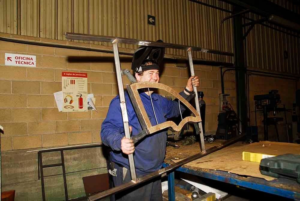 Un hombre que lleva una máscara de soldador sostiene un trozo de metal en una fábrica.