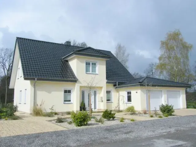 Großes cremefarbenes Haus mit dunklem Dach, Garage und Kiesauffahrt unter einem bewölkten Himmel