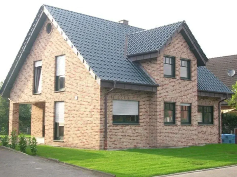 Modernes Backsteinhaus mit grauem Dach und grünem Rasen neben einer gepflasterten Auffahrt