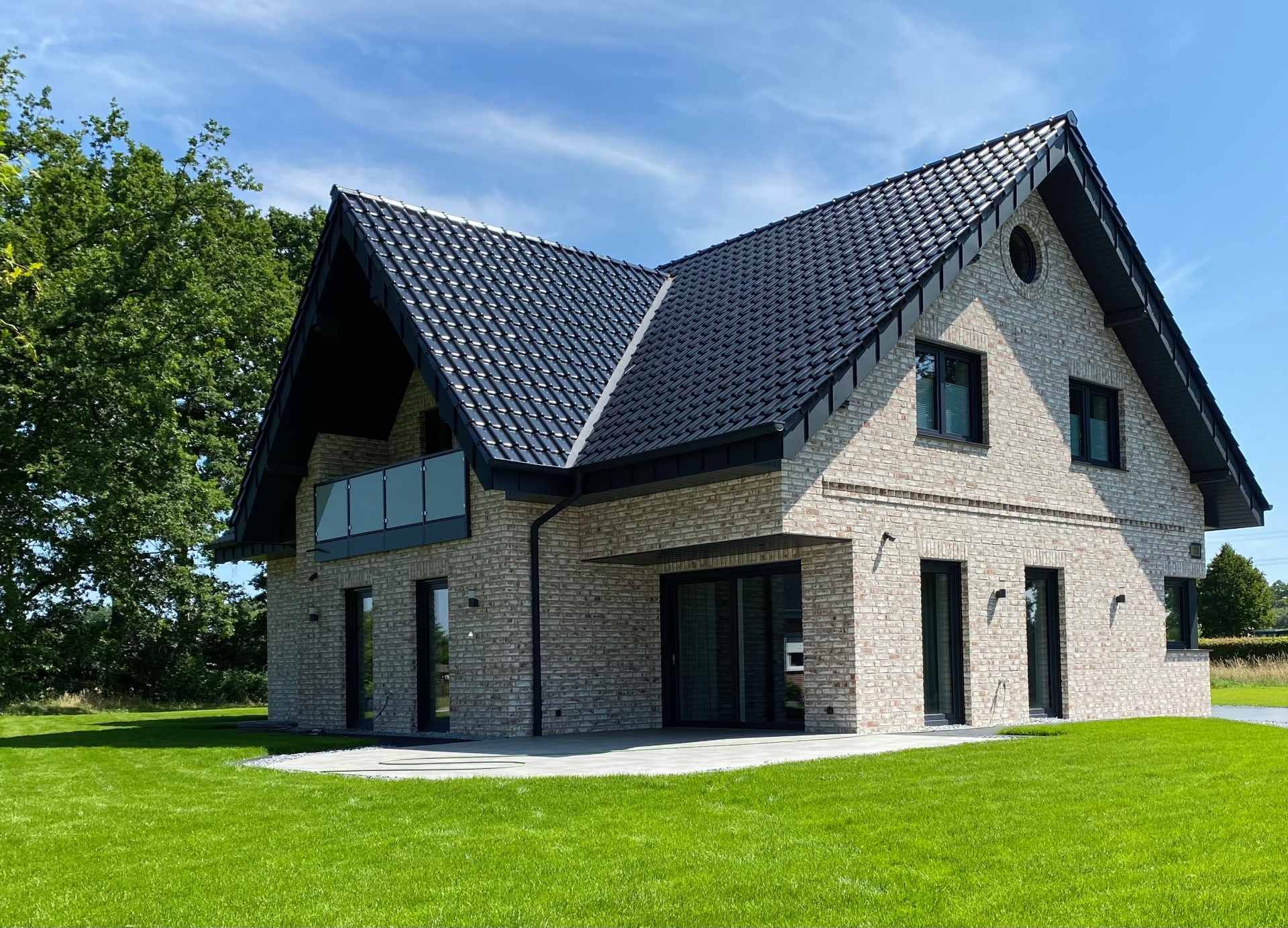 Modernes Steinhaus mit dunklem Dach und großen Fenstern auf einem grünen Rasen unter blauem Himmel