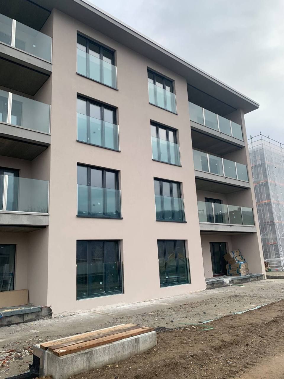 Edificio residenziale beige a più piani con balconi in vetro, infissi scuri e cielo nuvoloso.