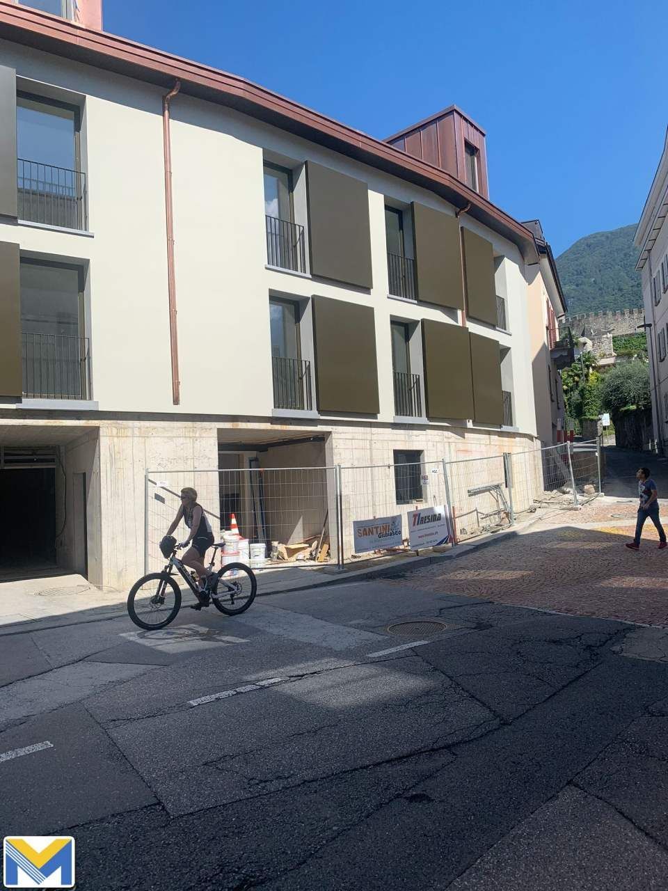 Un ciclista percorre una strada di fronte a un edificio con le persiane marroni. Lavori in corso davanti.