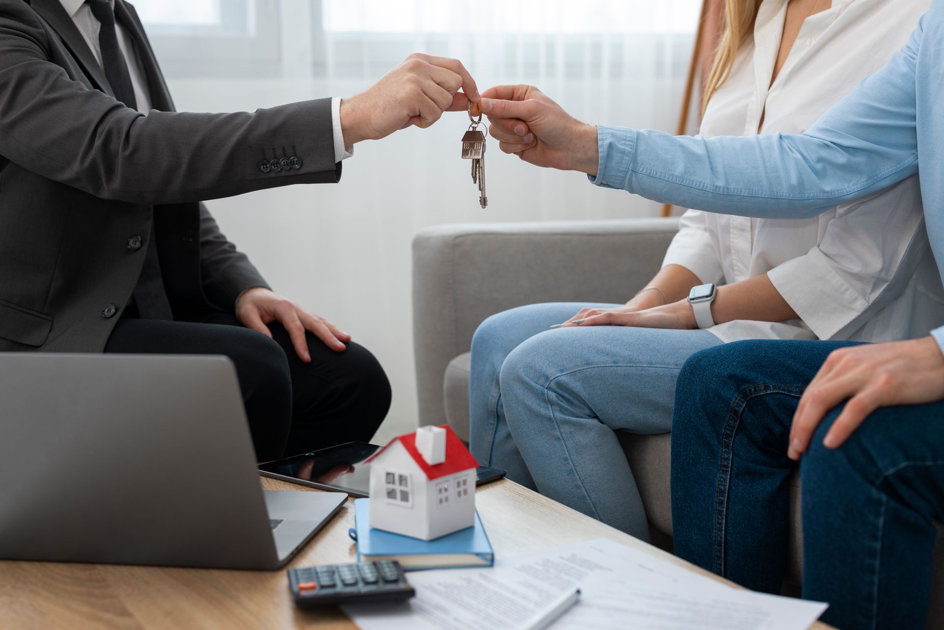 Agente inmobiliario entregando llaves de casa a una pareja sentada en un sofá.
