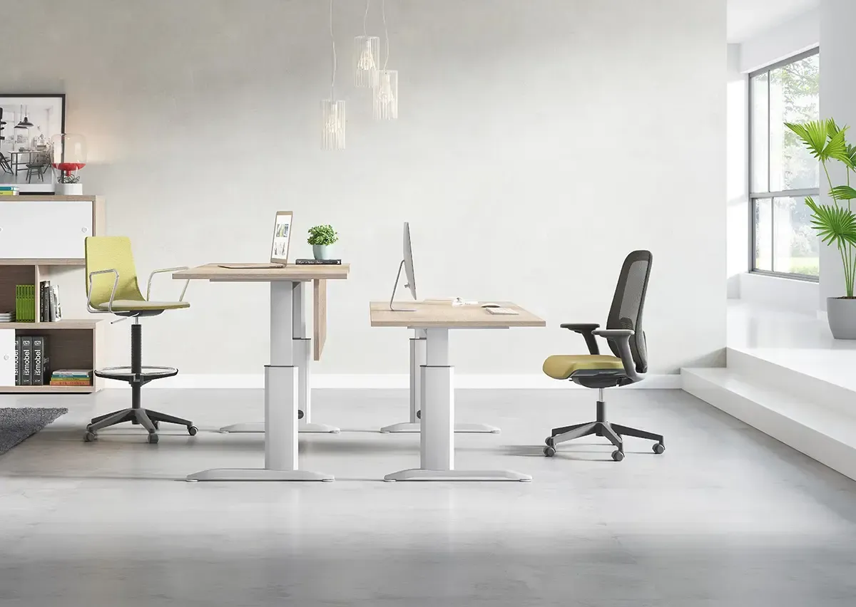 Dos escritorios de pie ajustables en una oficina moderna, con sillas de oficina y plantas en macetas.