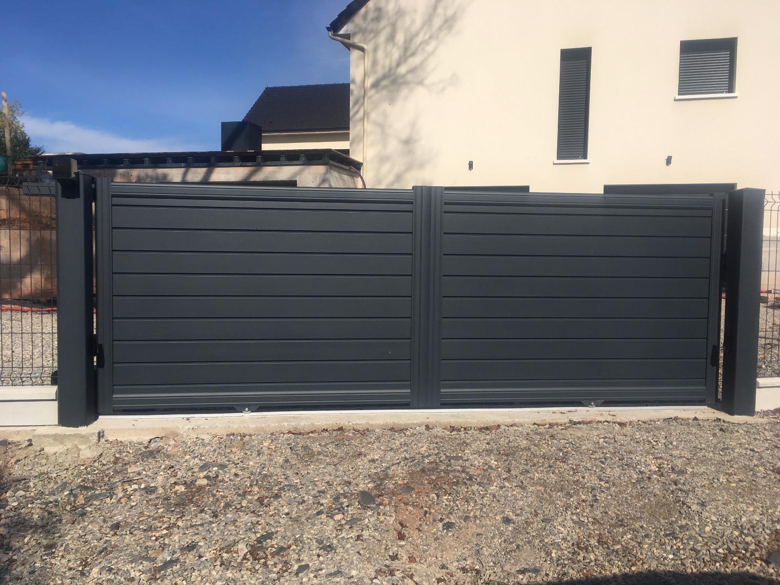 Portail à lattes horizontales gris foncé, fermé, devant une maison donnant sur une allée de gravier.