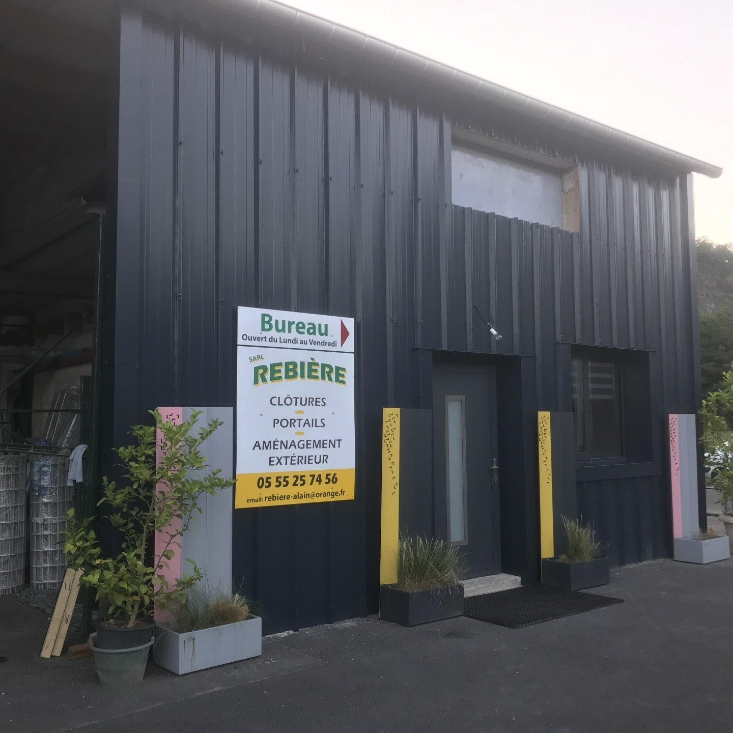 Bâtiment métallique gris foncé avec une porte, des fenêtres et une enseigne.
