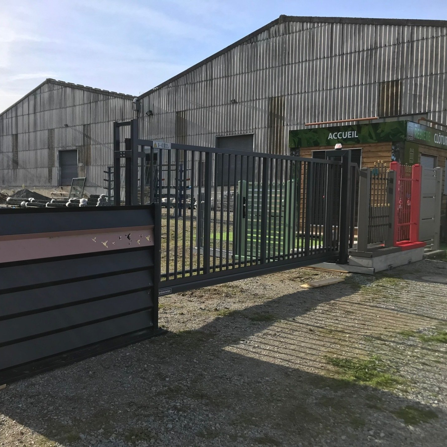 Un portail en métal sombre devant un bâtiment avec une petite structure en bois.