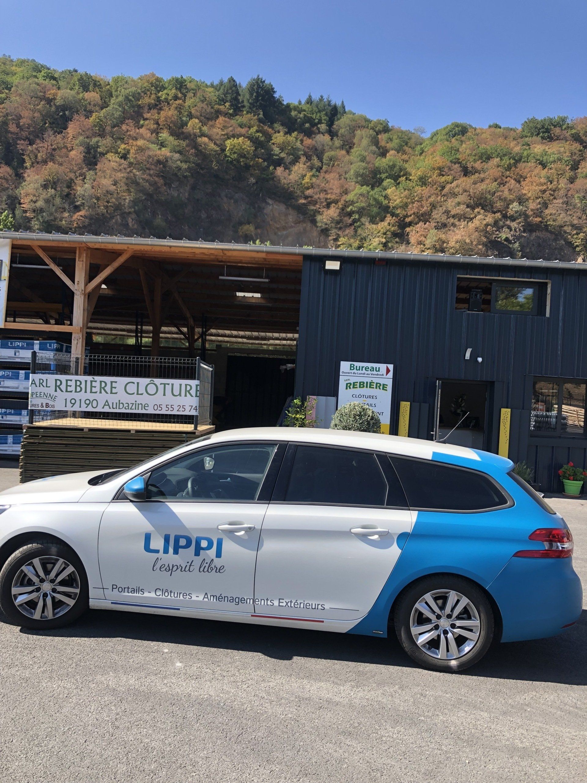 Voiture de la société Lippi, blanche et bleue, garée devant un entrepôt.