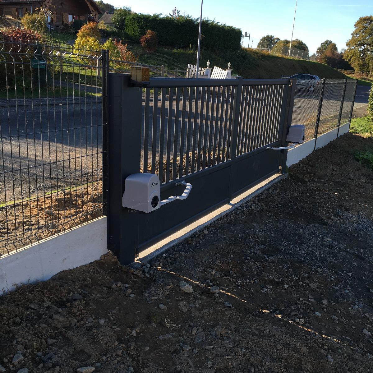 Portail automatique noir, partiellement ouvert, donnant sur une allée de gravier, entourée d'une clôture et de verdure.