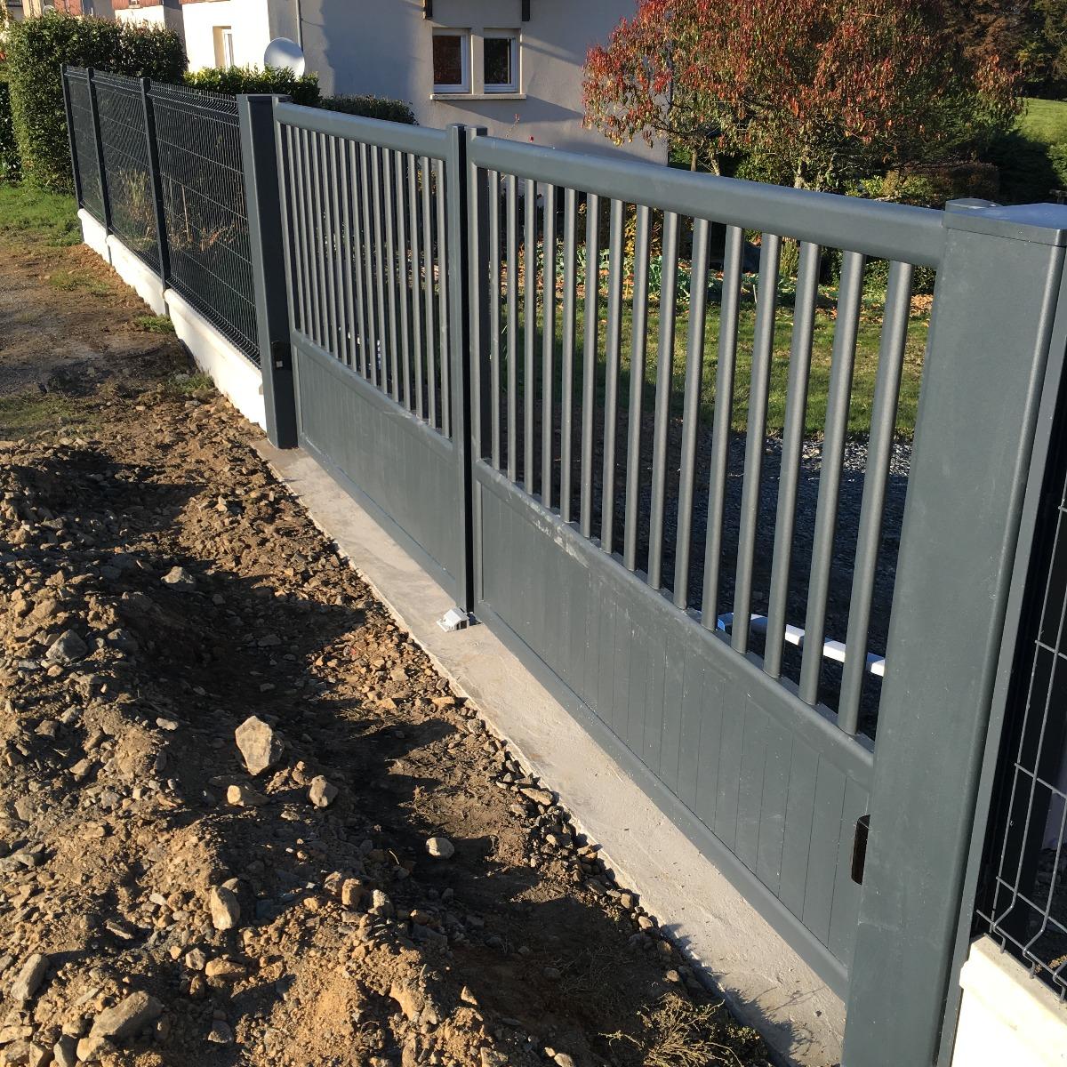 Portail et clôture en métal gris. Le portail se trouve devant une maison. Il est fermé et comporte des barreaux verticaux.