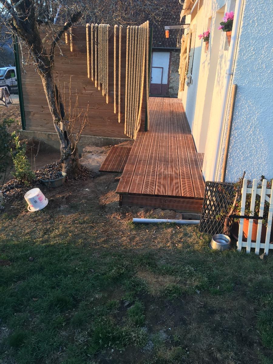 Une terrasse en bois et une corde s'étendent d'un bâtiment jusqu'à une cour.