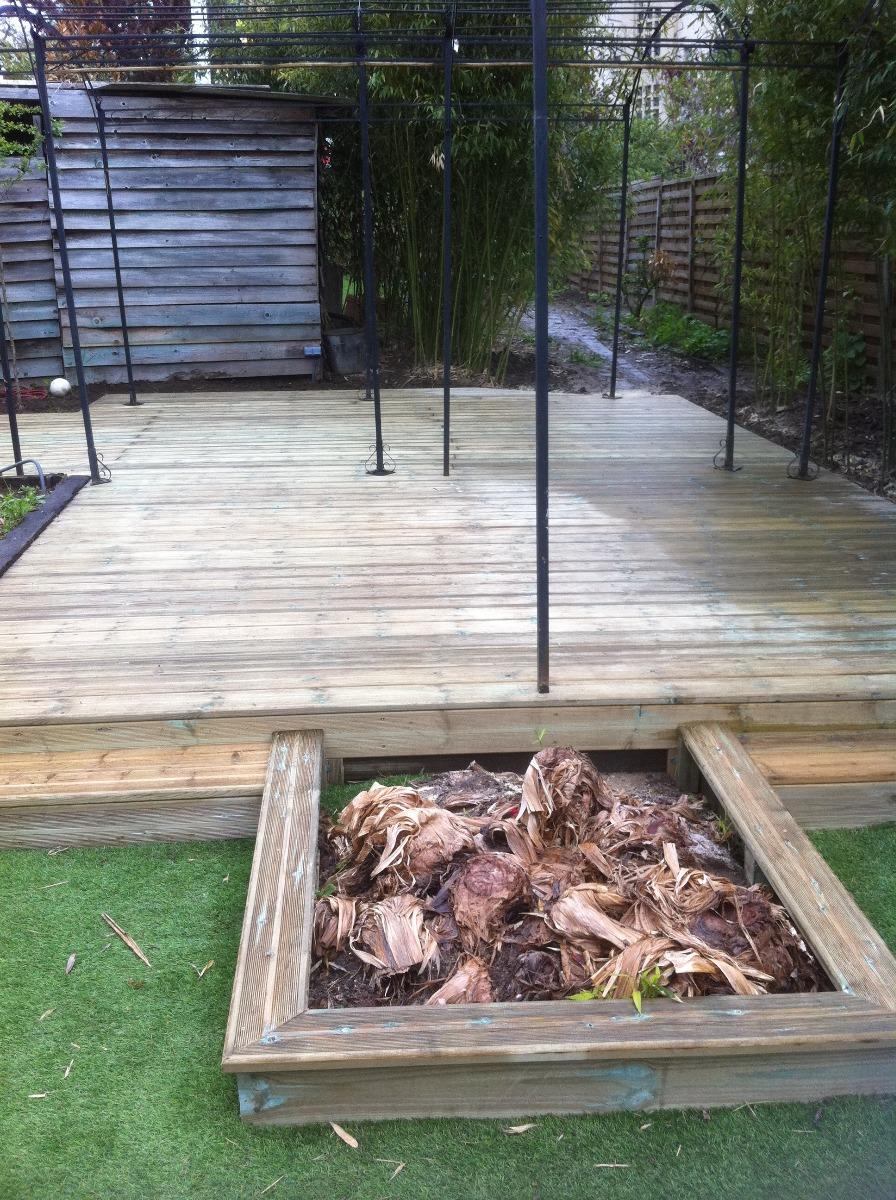 Terrasse en bois avec une zone surélevée, entourée de pelouse et d'un petit coffre en bois.