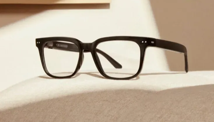 Gafas con montura negra sobre superficie color crema con sombras.