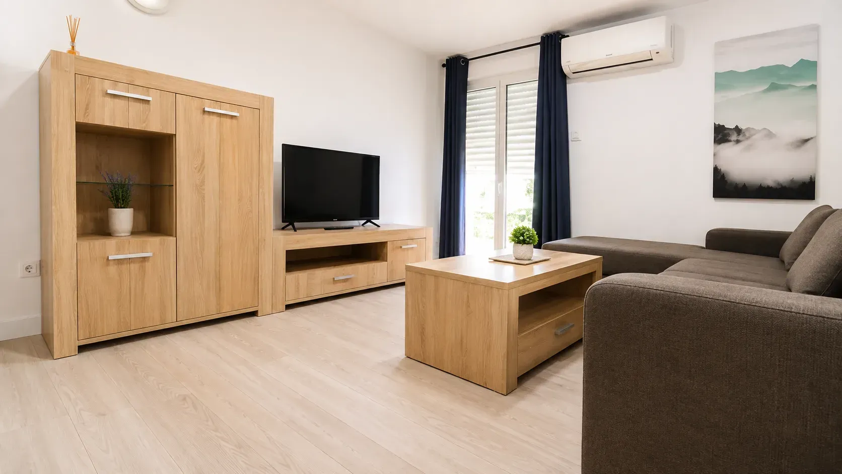 Sala de estar moderna con sofá marrón, televisor, mueble de madera, mesa de centro y grandes cortinas.