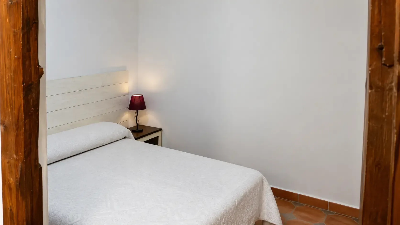 Acogedora habitación doble con dos camas blancas, lámpara cálida, ventana abierta y aire acondicionado de pared.