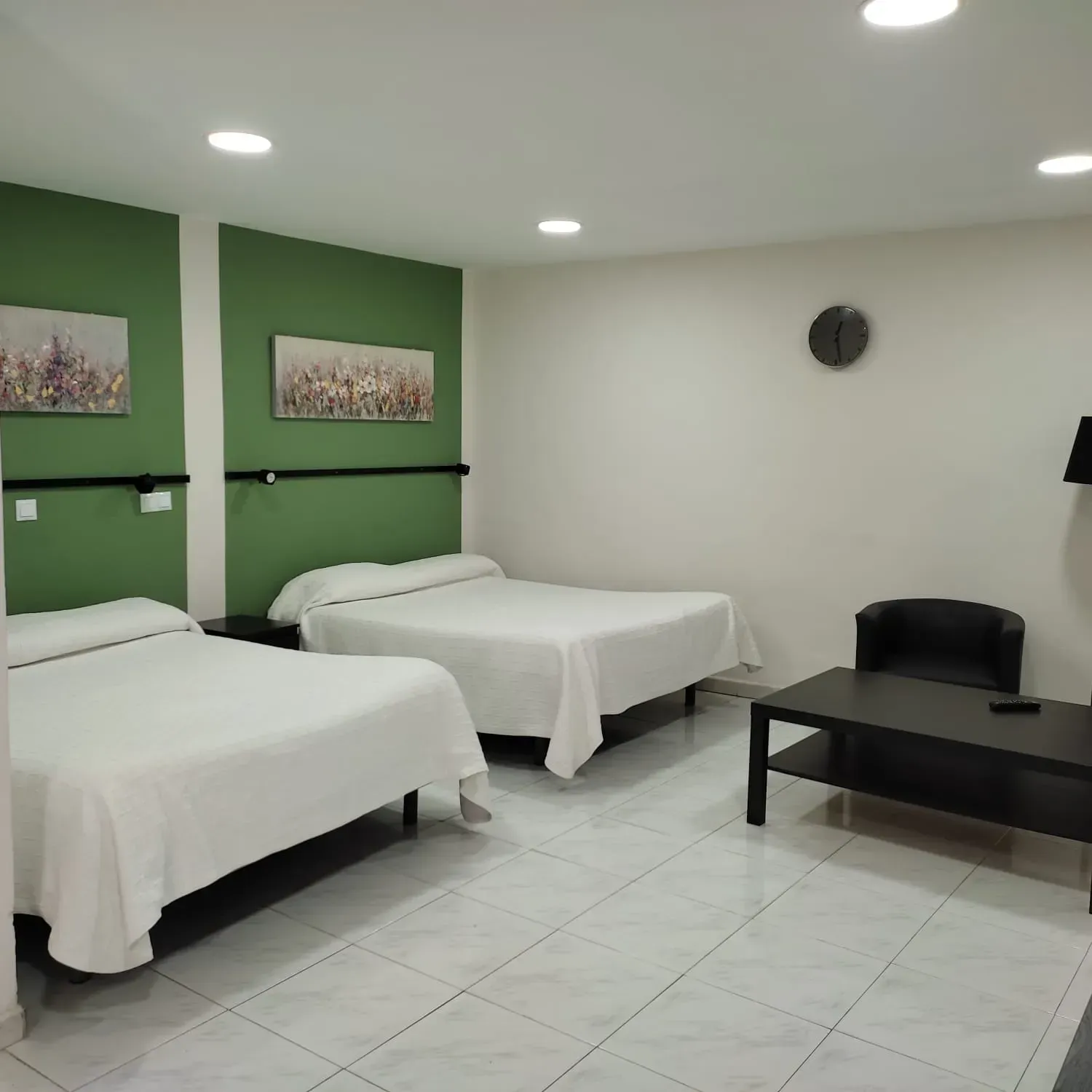 Habitación de hotel minimalista con dos camas blancas, paredes decorativas verdes, muebles negros y suelo de baldosas.